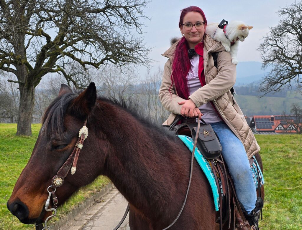 Reiterin mit Katze auf der Schulter unterwegs
