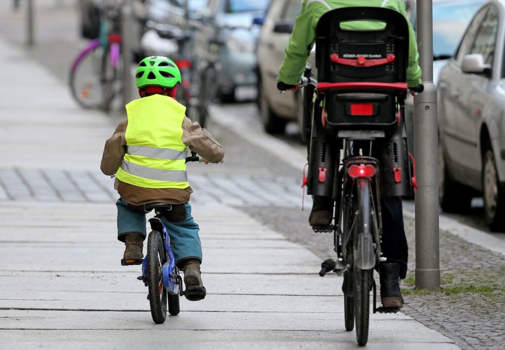 Ein Kind fährt mit dem Rad auf dem Fußweg neben einem Elternteil