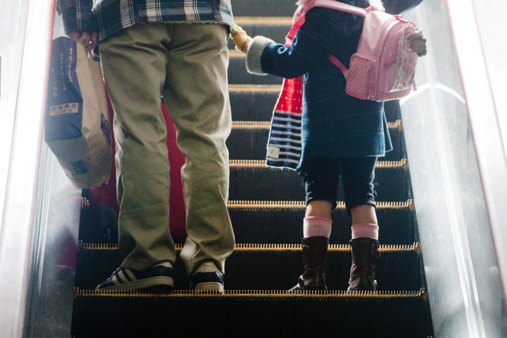 Mädchen steht neben ihrem Vater auf einer Rolltreppe