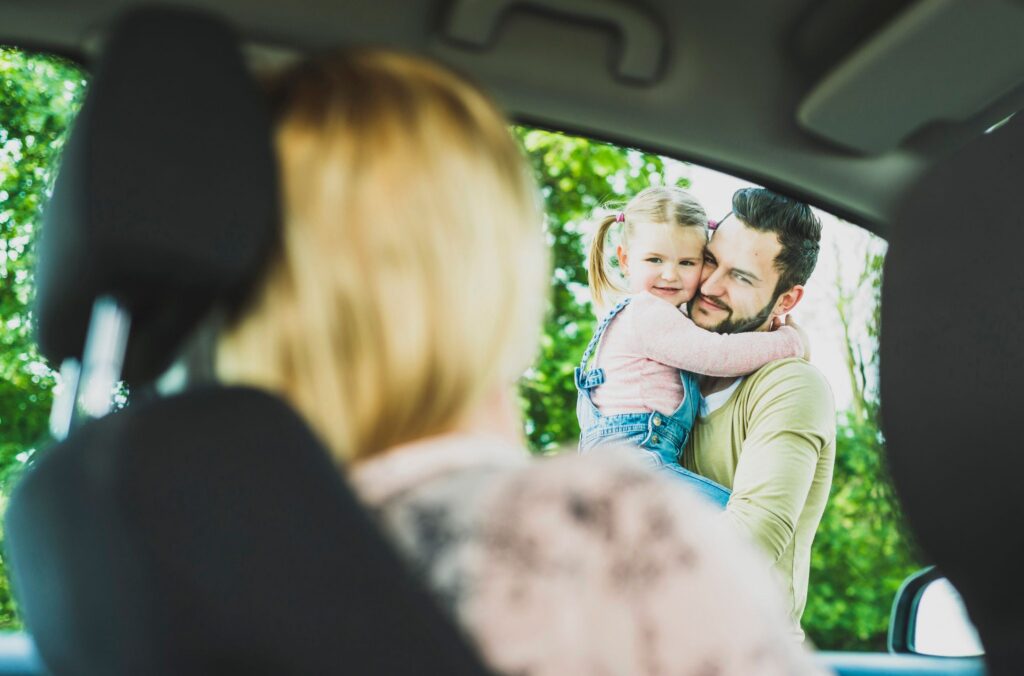 Vater mit Tochter auf dem Arm verabschieden Mutter im Auto