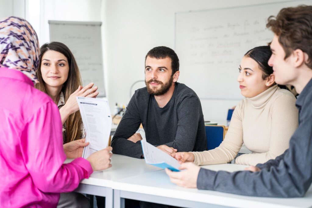 Fünf Erwachsene sitzen um einen Tisch in einem Klassenraum