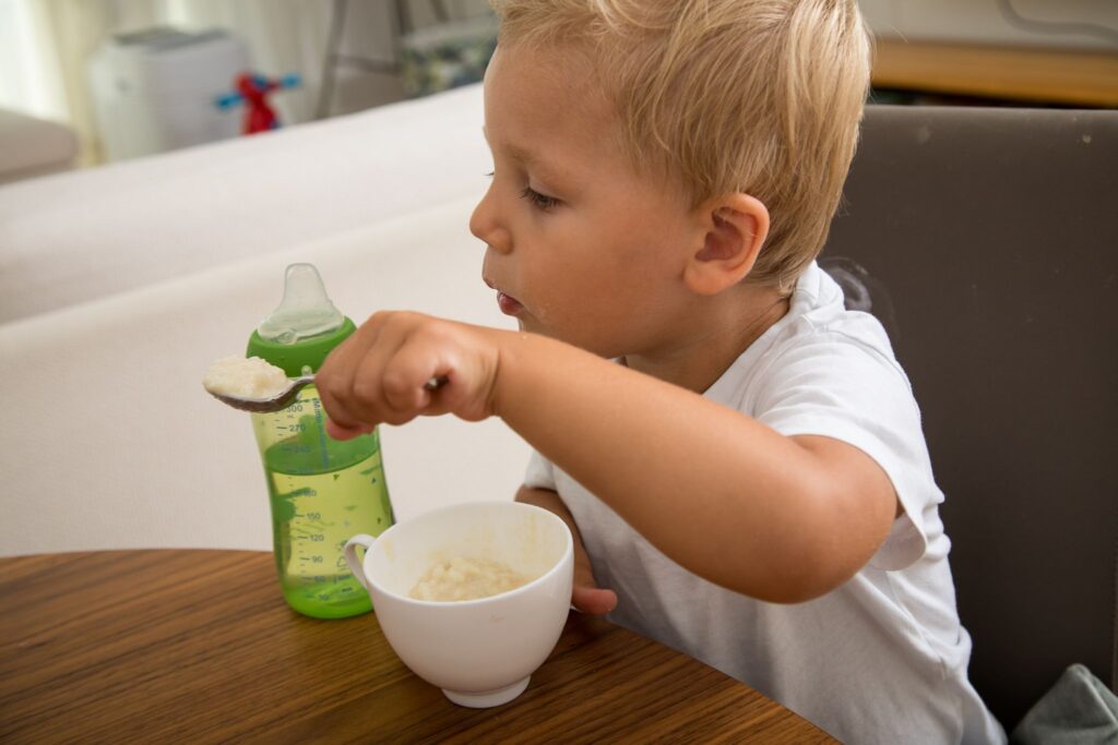 Ein kleiner Junge löffelt mit der linken Hand Milchreis