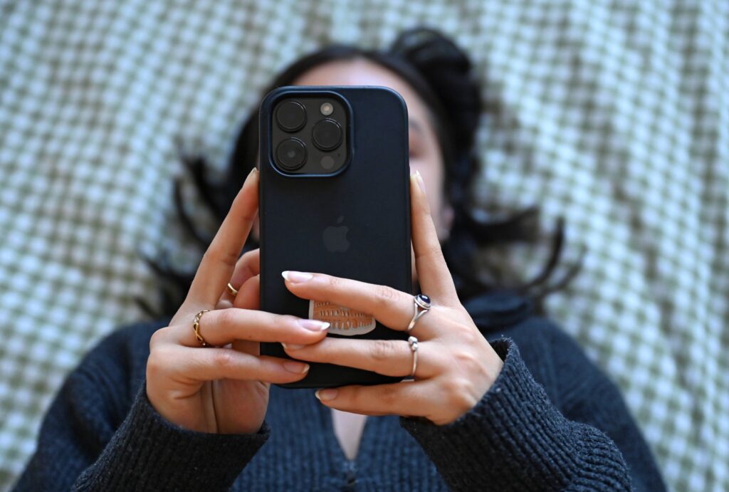 Eine junge Frau liegt mit dem Smartphone in der Hand auf dem Bett